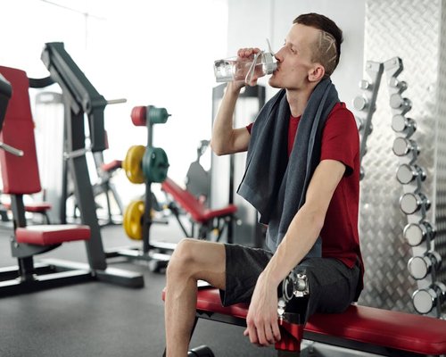 Person taking a rest break drinking water from a bottle in a gym
